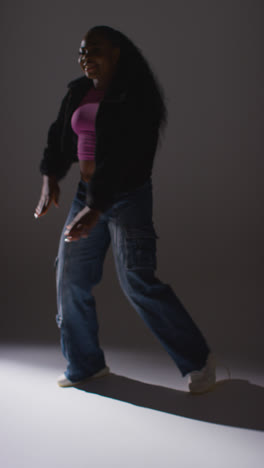 Vertical-Video-Studio-Portrait-Shot-Of-Young-Woman-Dancer-Wearing-Hoodie-Dancing-In-Against-Grey-Background-In-Slow-Motion